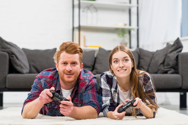 ビデオゲームで遊ぶカーペットの上に横たわる笑顔若いカップルの肖像画