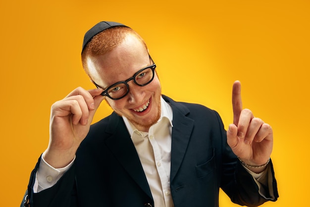 写真 ヤルムークのメガネとスーツを着た笑顔の若いユダヤ人の肖像画黄色に指を上げている
