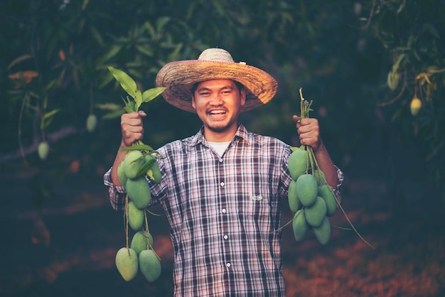 写真 木に生マンゴーを握っている笑顔の若い男の肖像画