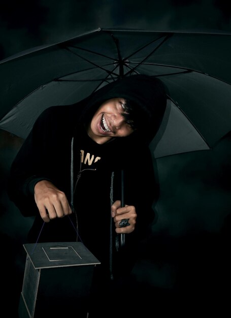写真 黒い背景に立って傘を握っている笑顔の若い男の肖像画