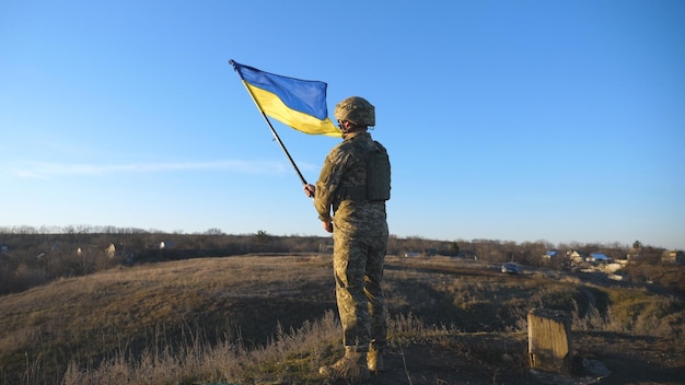 Фото Портрет солдата в военной форме поднял флаг украины на холме мужчина украинской армии держит размахивающий флагом победа над российской агрессией концепция сопротивления вторжению медленное движение