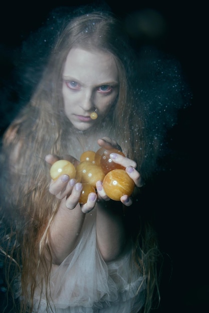 写真 黒い背景に果物を飾った恐ろしい若い女性の肖像画