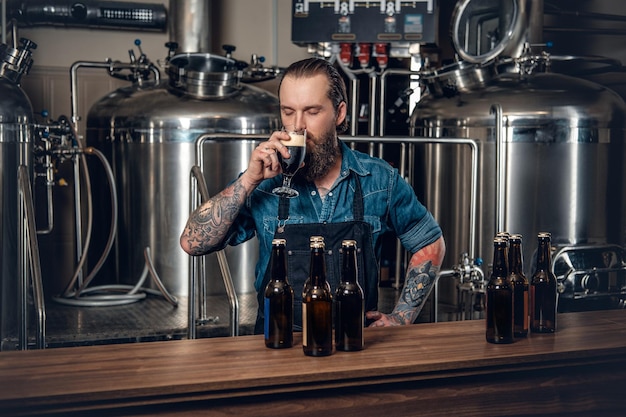 写真 地ビール醸造所でビールを味わう入れ墨、ひげを生やしたヒップスターの男性メーカーの肖像画。