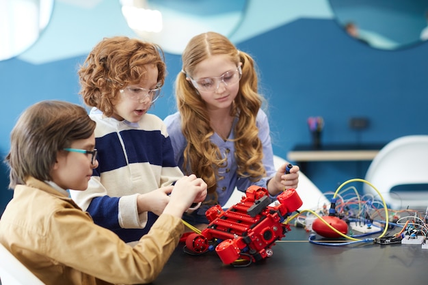 Портрет трех симпатичных детей, которые вместе строят робота, наслаждаясь уроками инженерии в школе развития