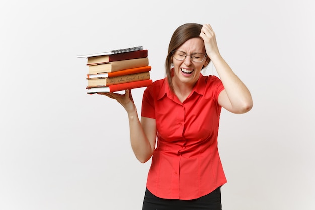 白い背景で隔離の手でスタック教科書を保持している赤いシャツのメガネで疲れた欲求不満の動揺ビジネス教師の女性の肖像画。高校の大学の概念における教育または教育。