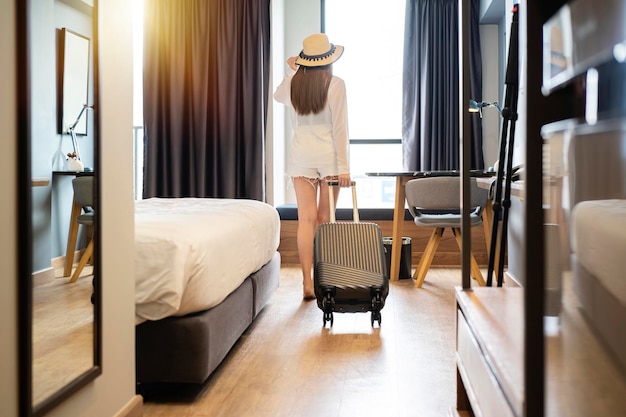 Фото Портрет туристки, стоящей у окна и смотрящей на прекрасный вид со своим багажом в спальне отеля