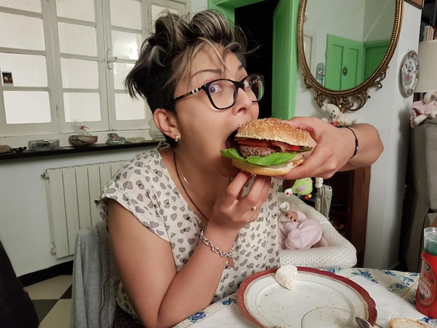 写真 テーブルに座ってハンバーガーを食べている女性の肖像画