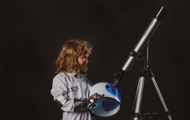 Фото Портрет удивленного маленького астронавта в шлеме и защитном скафандре с успехом в телескопе
