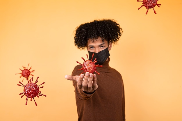 Фото Портрет молодого афро-мальчика волос с медицинской маской на желтом фоне, держащего бактериальную молекулу. эпидемия, вирус, здоровье. копировать пространство