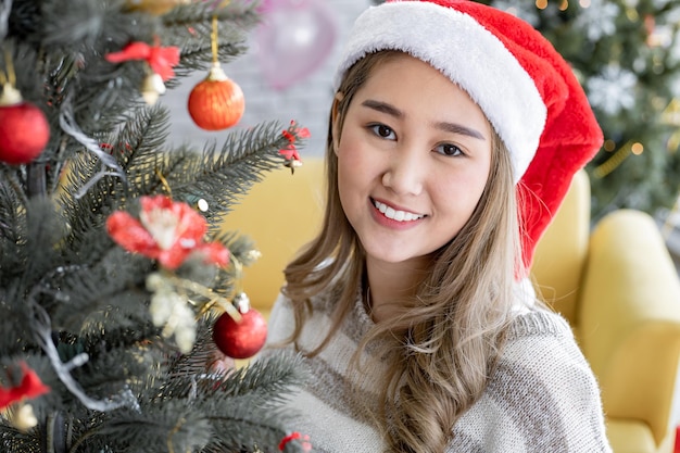 写真 幸せな休日に自宅で笑顔でクリスマスのお祝いのクリスマスツリーを飾る若いアジアのかわいい女性の肖像画。クリスマスフェスティバルと新年に幸せです。