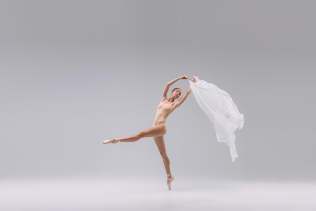 Фото Портрет молодой балерины, танцующей с белой прозрачной тканью, изолированной над серой студией
