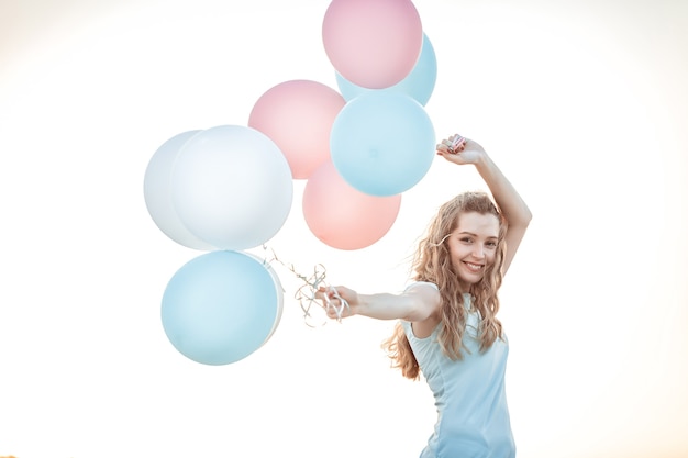Фото Портрет молодой красивой женщины с летающими разноцветными воздушными шарами на фоне неба