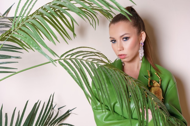 Фото Портрет молодой красивой женщины с идеальной гладкой кожей в тропических листьях в зеленой кожаной куртке ...