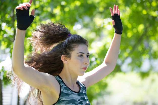 写真 夏の公園でスポーツウェアのトレーニングで長い巻き毛を持つ若いブルネットの女性の肖像画