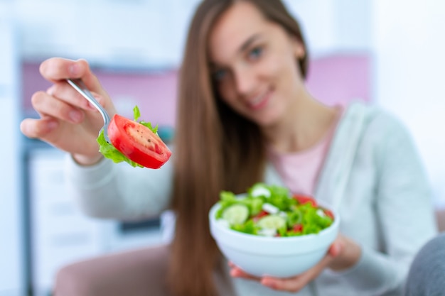 自宅で新鮮な野菜サラダを食べる若い幸せな健康な女性の肖像画