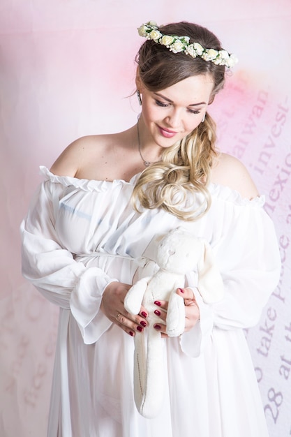 Портрет молодой счастливой беременной женщины, позирующей с плюшевым мишкой
