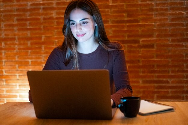 Фото Портрет молодой счастливой женщины, использующей ночной ноутбук с использованием современных технологий, веселящейся с светящимся экраном в темном офисе или дома.