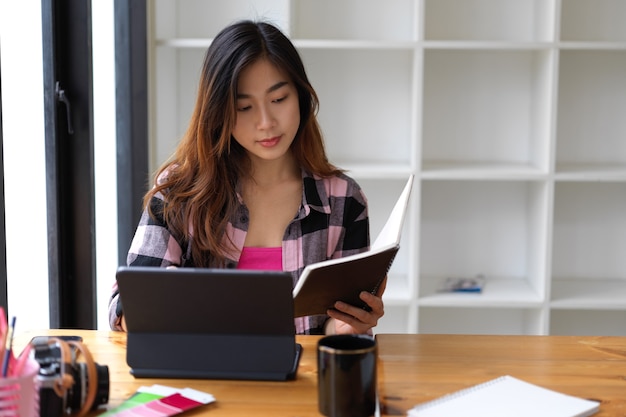 事務室でタブレットを操作しながらノートを読んでいる若い素敵な女性の肖像画