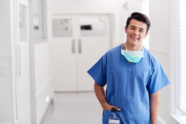 写真 病院の廊下に立っているスクラブを身に着けている若い男性医師の肖像画