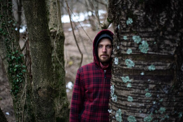 Фото Портрет молодого человека, стоящего у ствола дерева в лесу