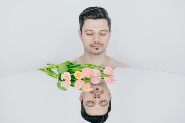 Фото Портрет молодого человека с зеркалом и цветами на белом фоне