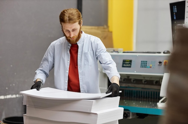 Фото Портрет молодого человека, работающего в типографии и держащего стопку бумаги для копирования