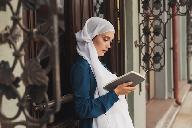 屋外で本を読んでヒジャーブを身に着けている若いイスラム教徒の女性の肖像画