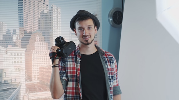 Фото Портрет молодого фотографа в повседневной одежде с профессиональной камерой, улыбаясь и позирует