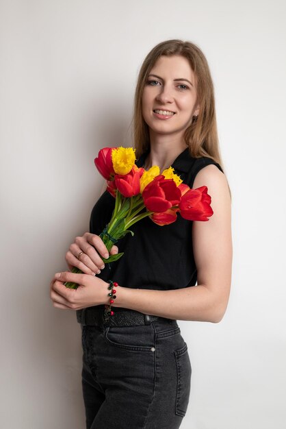 Фото Портрет молодой красивой женщины, улыбающейся и держащей красивый букет цветов красных тюльпанов на белом