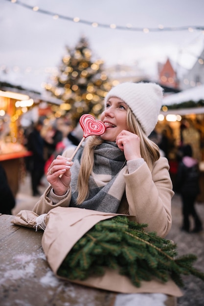 写真 クリスマスマーケットでハート形のロリポップを舐める若い笑顔の女性の肖像画