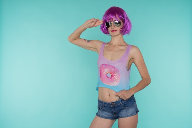 Портрет молодой трансгендерной женщины с проблемной кожей в розовом парике и солнцезащитных очках в форме сердца на синем фоне