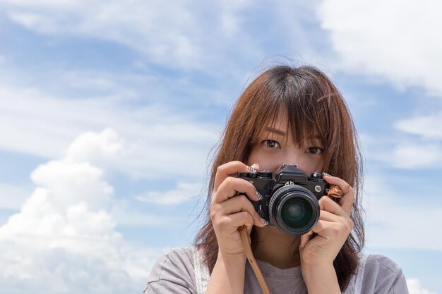 写真 雲の空を背景にカメラを握っている若い女性の肖像画