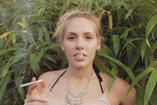 写真 植物に立ってマリファナを吸っている若い女性の肖像画