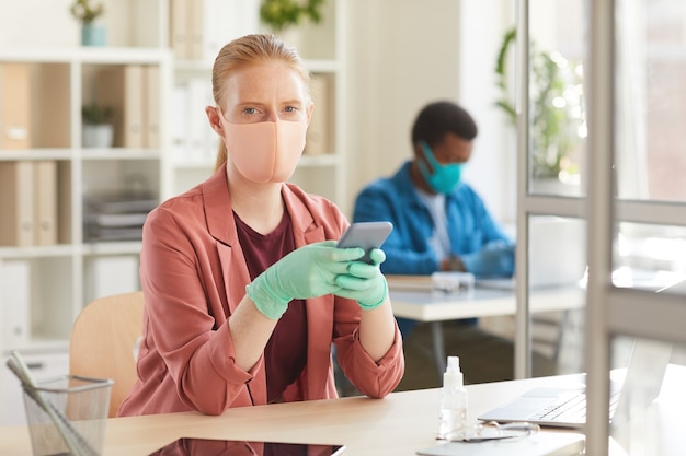 Фото Портрет молодой женщины в маске и перчатках, работающей за столом в кабинке в офисе после пандемии