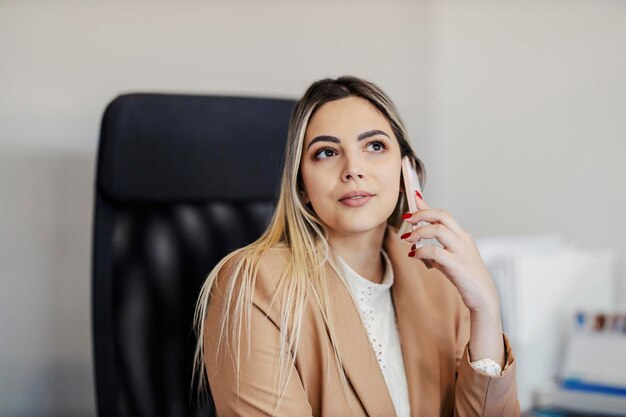 Portrait of a office assistant sitting at her workspace and having phone call