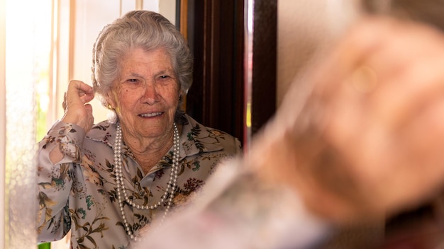 Photo portrait of old caucasian woman looking at mirror in living room grandmother