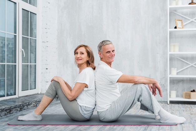 Portrait of a old couple sitting back to back on yoga mat