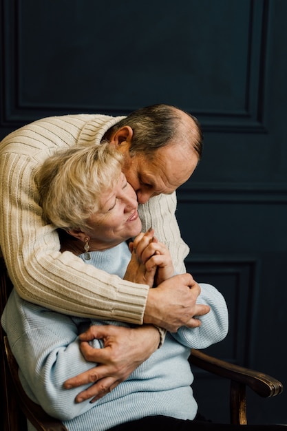 Portrait of old couple wife and husband hugging and smiling. Dark blue background. Happy lovers on