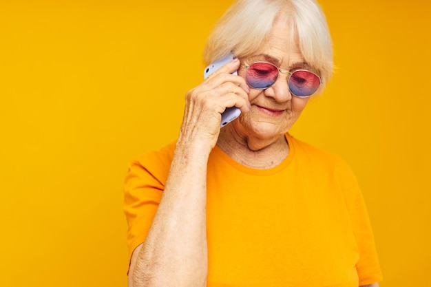 電話の黄色の背景でカジュアルなTシャツのコミュニケーションで古いフレンドリーな女性の肖像画
