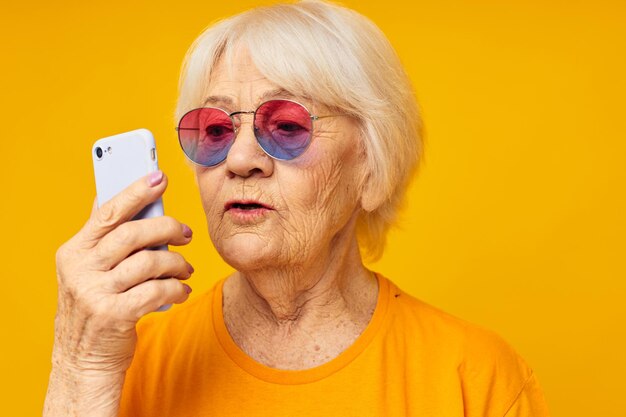 Portrait of an old friendly woman in fashionable glasses with a smartphone isolated background