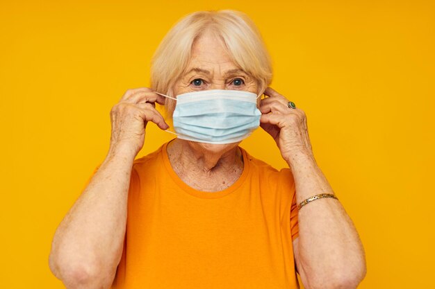 Portrait of an old friendly woman in yellow tshirts in medical masks yellow background