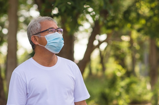 Il ritratto dell'uomo anziano indossa la maschera chirurgica in un parco all'aperto