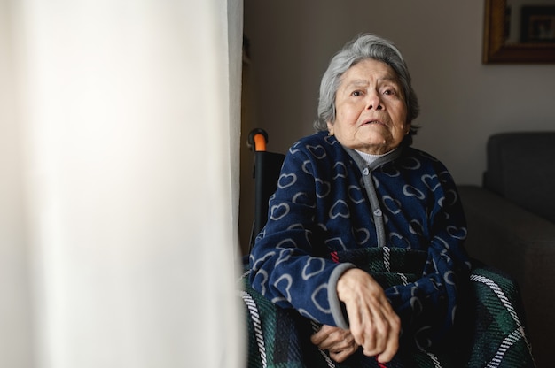 Portrait old sick woman sitting in wheelchair at home with\
disoriented, confused face.. third age, home elderly assistance\
concept.