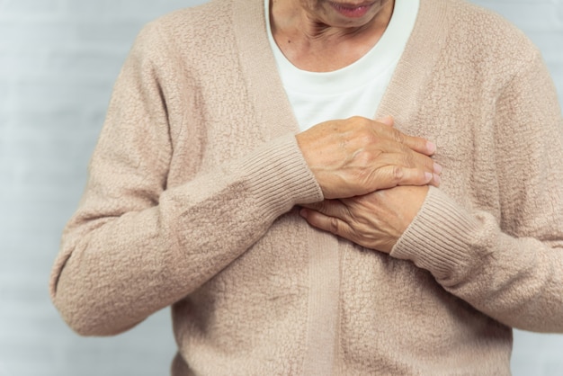 Portrait of old woman holding breast because of heart infarction on gray 