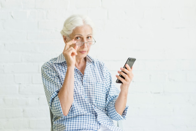 Photo portrait of an old woman holding smartphone in front of white wall