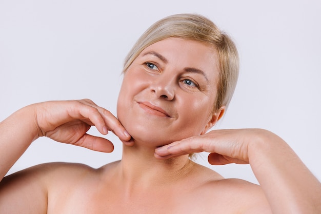 Portrait of an old woman who quite touches the delicate and clean skin of her face with her hands on