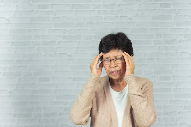 Portrait of old woman with headache on gray 