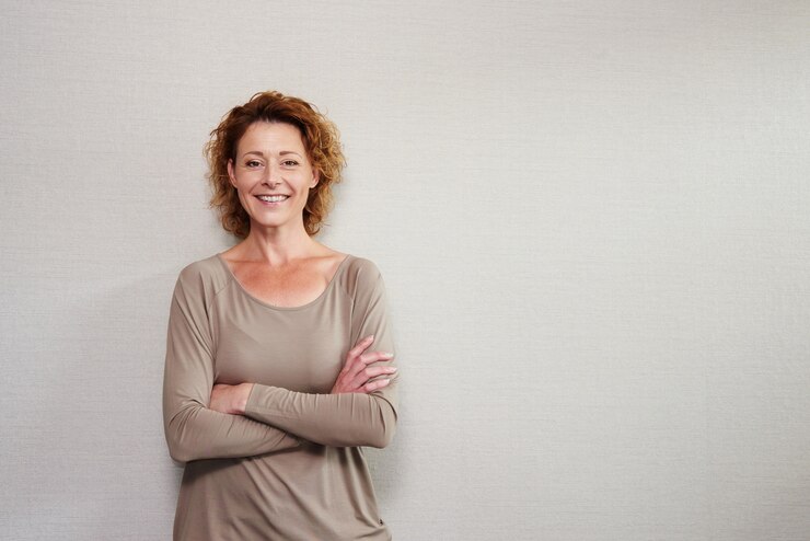 Photo portrait of older woman smiling with arms crossed by wall