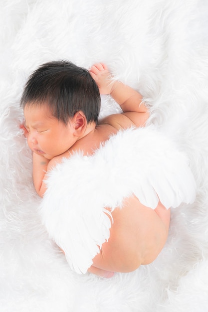 Portrait of a one month old sleeping, newborn baby girl. She is wearing a feather angel wings, and sleeping on a white blanket. Concept portrait studio fashion newborn.