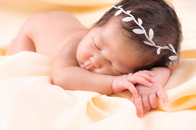 Portrait of a one month old sleeping, newborn baby girl. She is wearing a white crown headband and sleeping on a cream blanket. Concept portrait studio fashion newborn.